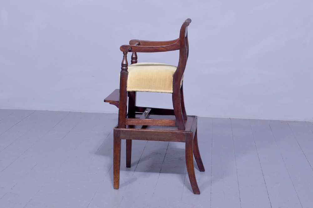 A George III mahogany childs high chair with a gold upholstered seat, safety bar, and footrest, resting atop a matching wooden stand. View III