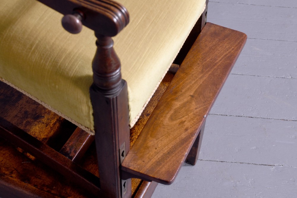 A George III mahogany childs high chair with a gold upholstered seat, safety bar, and footrest, resting atop a matching wooden stand. View IV