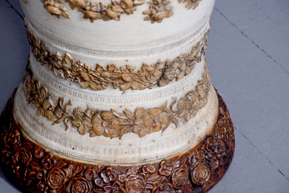 A Victorian glazed stoneware water filter urn decorated with relief crest motifs, floral borders, side handles, and a fitted wooden lid. View II