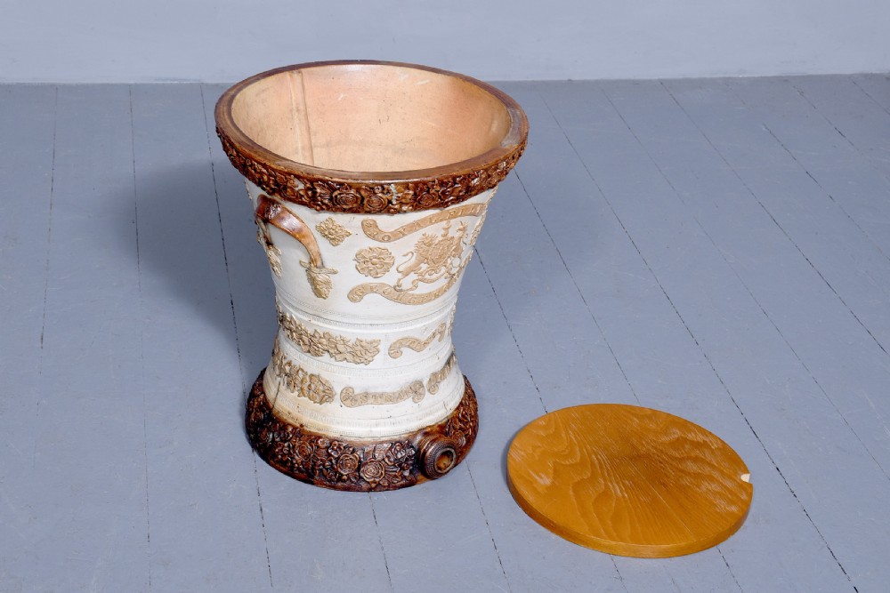 A Victorian glazed stoneware water filter urn decorated with relief crest motifs, floral borders, side handles, and a fitted wooden lid. View VII