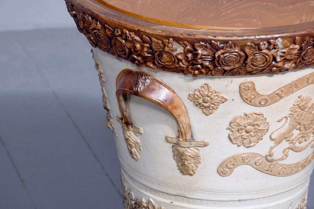 A Victorian glazed stoneware water filter urn decorated with relief crest motifs, floral borders, side handles, and a fitted wooden lid. View VIII