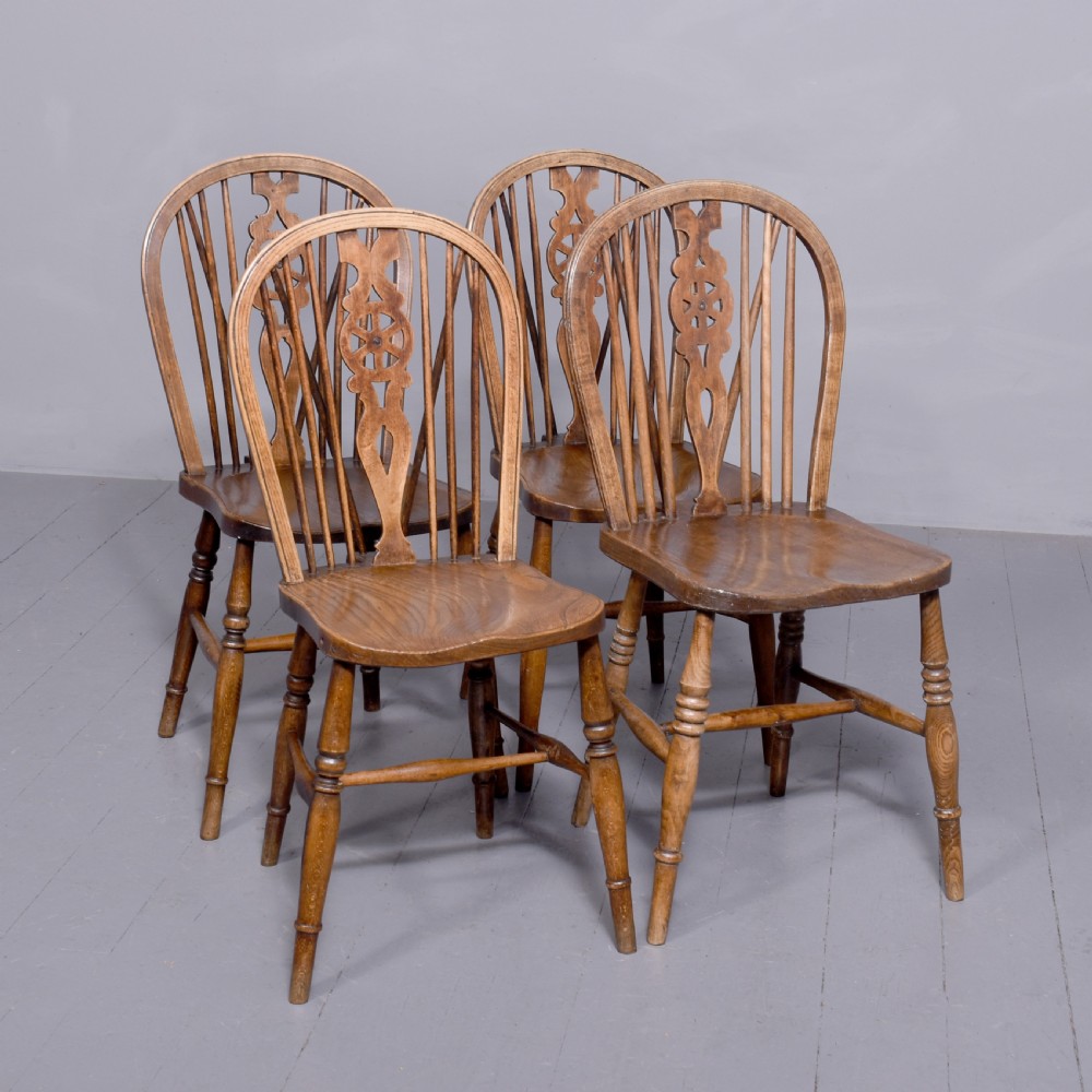 A set of four antique wooden Windsor dining chairs featuring hoop backs, pierced wheelback splats, shaped seats, and turned legs.