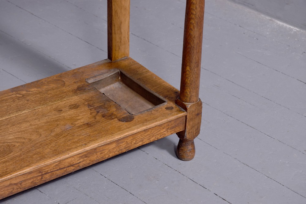 An antique oak Art Nouveau hall stand featuring a central mirror, brass coat hooks, a small shelf compartment, and a lower umbrella stand base. View V