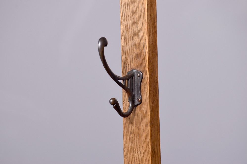An antique oak Art Nouveau hall stand featuring a central mirror, brass coat hooks, a small shelf compartment, and a lower umbrella stand base. View VII