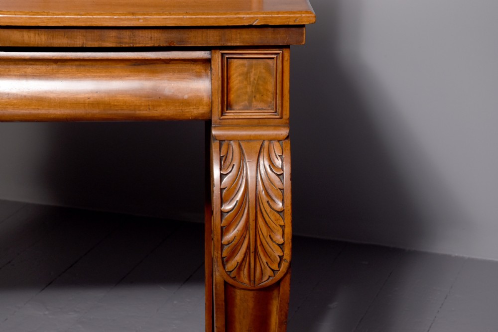A William IV mahogany console table featuring a pedimented upstand, flame mahogany frieze, and acanthus leaf carved scroll front legs resting on plinth bases. View III