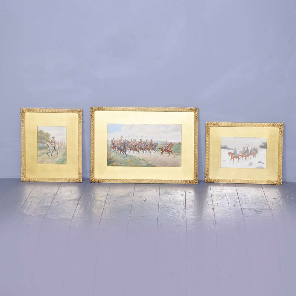 A set of three gilt-framed watercolour paintings depicting cavalry soldiers on horseback in varied rural landscapes.