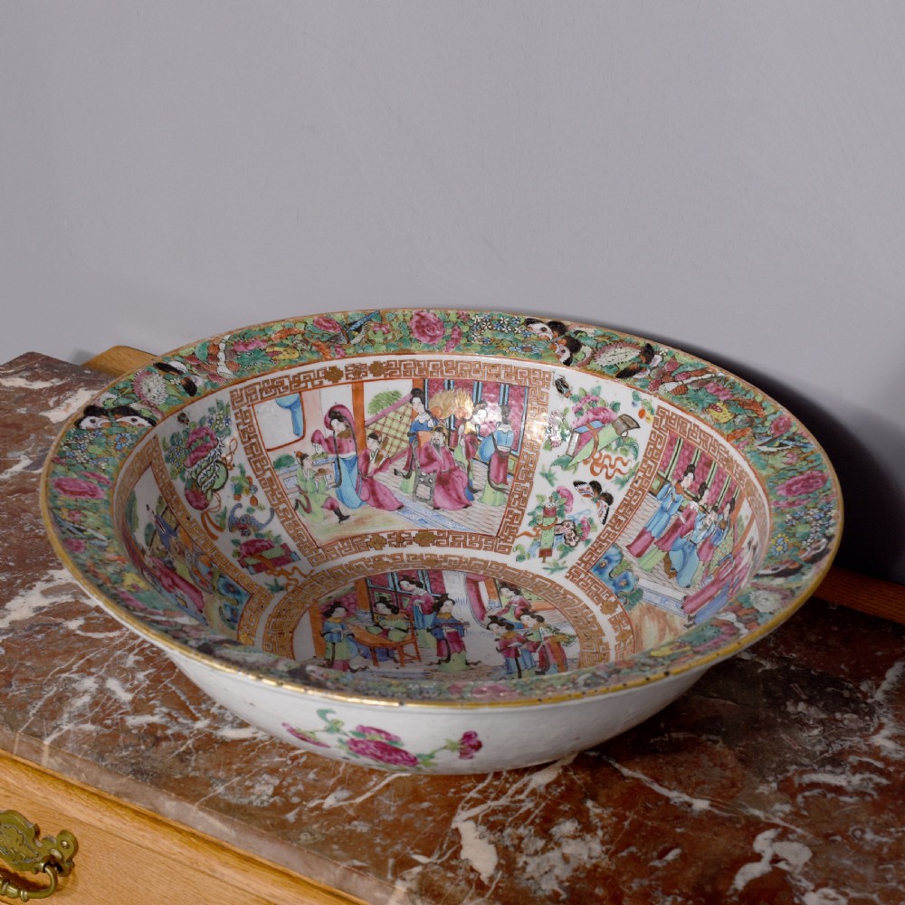 A large round Canton Famille Rose porcelain bowl decorated inside with hand-painted Mandarin figure scenes, floral borders, and gilded rims.