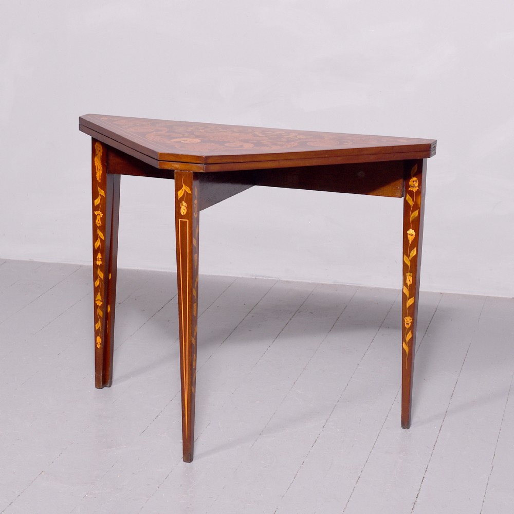 A triangular wooden Dutch card table featuring detailed floral marquetry inlay on the top surface and tapered square legs.