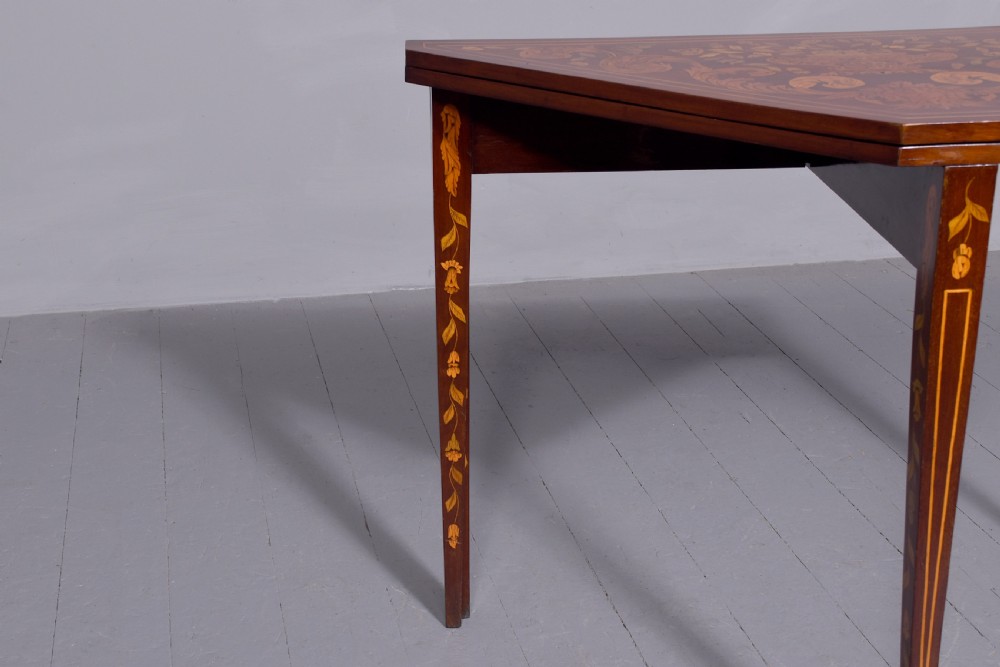 A triangular wooden Dutch card table featuring detailed floral marquetry inlay on the top surface and tapered square legs. View III