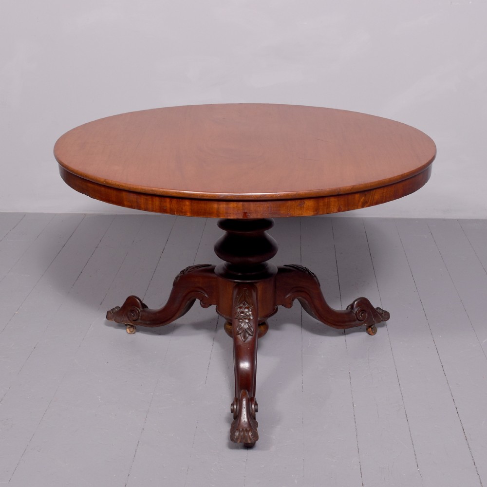 A Victorian circular mahogany table featuring a polished top, a central turned pedestal stem, and carved quadruped legs with castors.