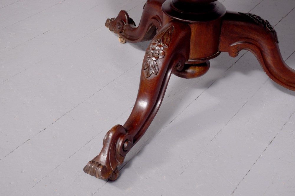 A Victorian circular mahogany table featuring a polished top, a central turned pedestal stem, and carved quadruped legs with castors. View II