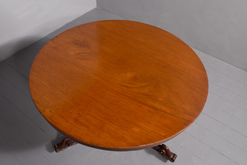 A Victorian circular mahogany table featuring a polished top, a central turned pedestal stem, and carved quadruped legs with castors. View III