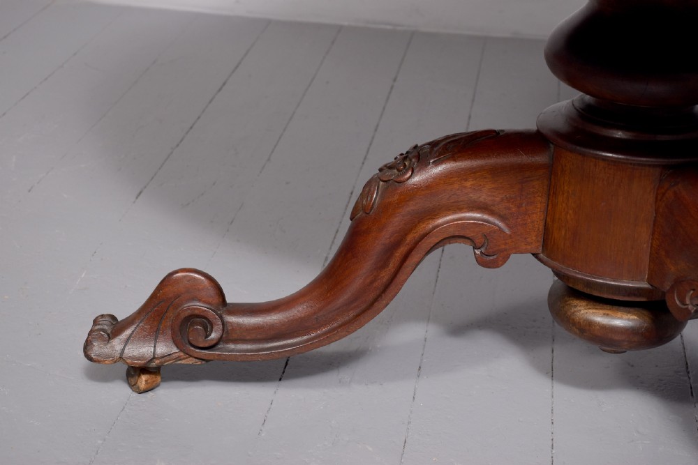 A Victorian circular mahogany table featuring a polished top, a central turned pedestal stem, and carved quadruped legs with castors. View IV