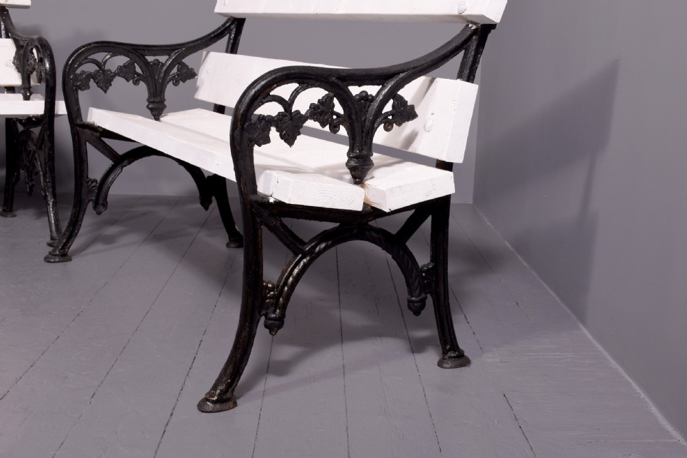 A pair of Victorian garden benches featuring dark cast iron side frames with ornate foliage scrollwork and white painted timber slatted seats and backs. View II