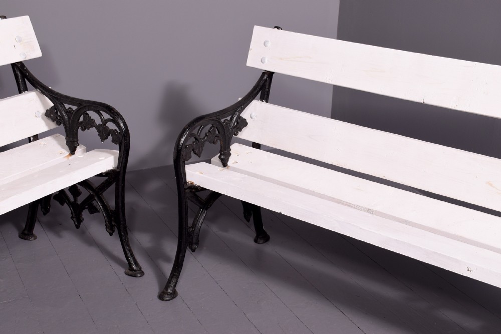 A pair of Victorian garden benches featuring dark cast iron side frames with ornate foliage scrollwork and white painted timber slatted seats and backs. View III