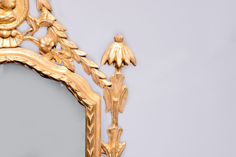 A late 18th-century Neoclassical giltwood wall mirror with a carved ribbon crest, profile medallion, and side foliate columns. View II