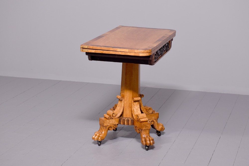 A George IV birdseye maple fold-over tea table featuring rosewood crossbanding, a central pedestal, and carved lion paw feet on brass castors. View II