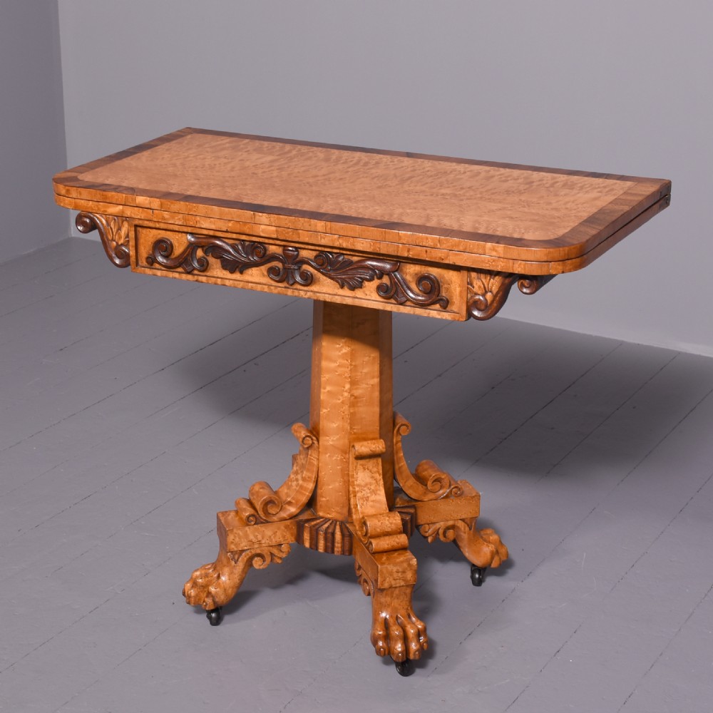A George IV birdseye maple fold-over tea table featuring rosewood crossbanding, a central pedestal, and carved lion paw feet on brass castors. View III