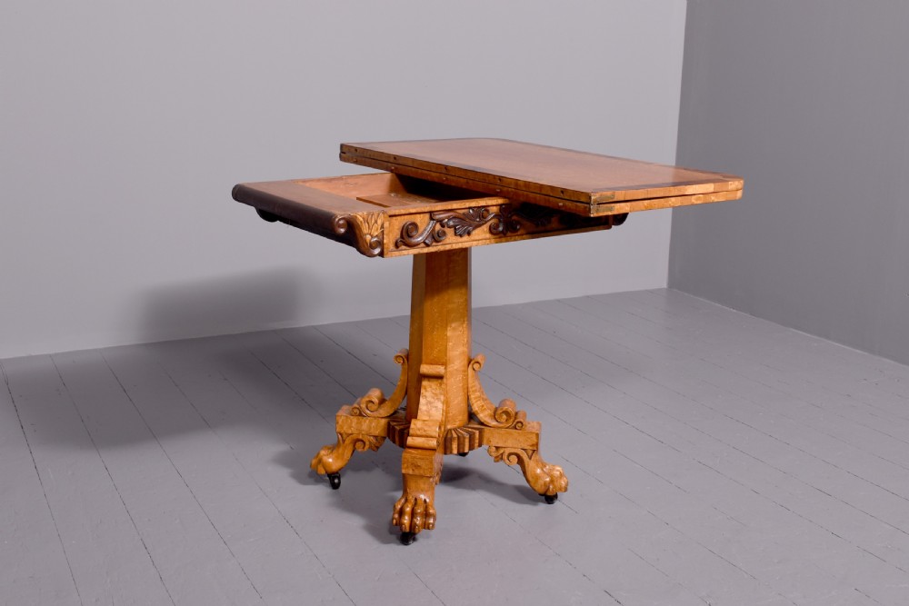 A George IV birdseye maple fold-over tea table featuring rosewood crossbanding, a central pedestal, and carved lion paw feet on brass castors. View V