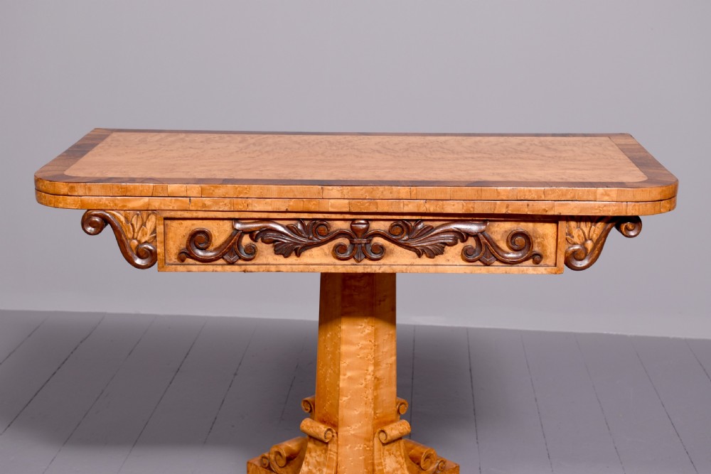 A George IV birdseye maple fold-over tea table featuring rosewood crossbanding, a central pedestal, and carved lion paw feet on brass castors. View VI