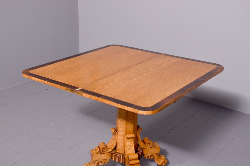 A George IV birdseye maple fold-over tea table featuring rosewood crossbanding, a central pedestal, and carved lion paw feet on brass castors. View VII