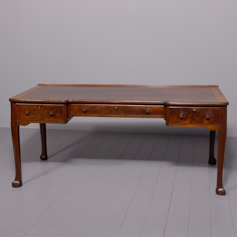 A large crossbanded mahogany library desk featuring three frieze drawers and slender cabriole legs.