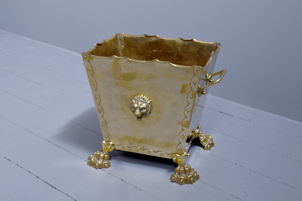 A rectangular Victorian brass coal bucket featuring scalloped edges, side handles, a central lion mask motif, and four cast paw feet. View V