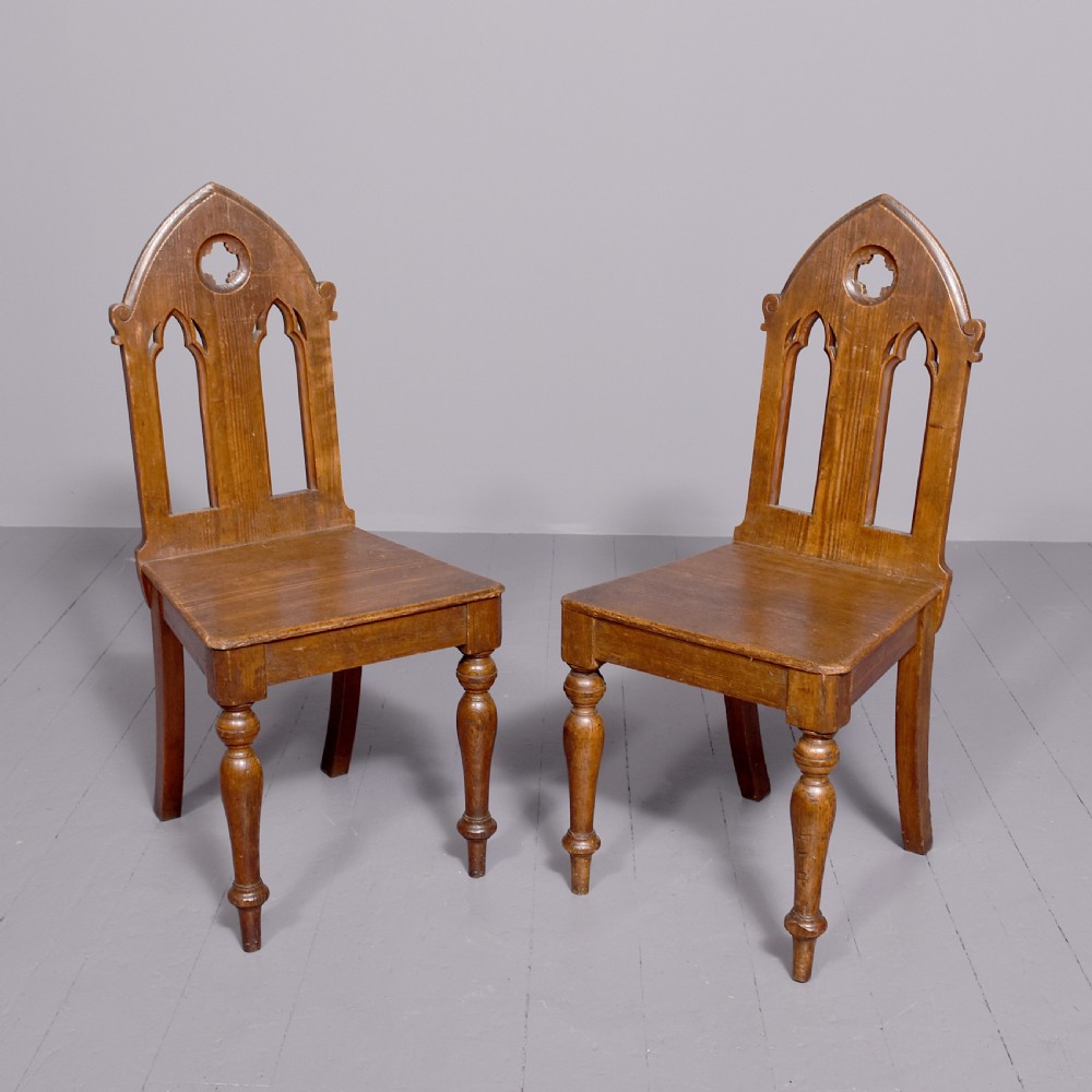 A pair of 19th-century pitch pine Gothic Revival hall chairs with pointed arch backrests, pierced trefoil motifs, turned front legs, and solid timber seats. View II