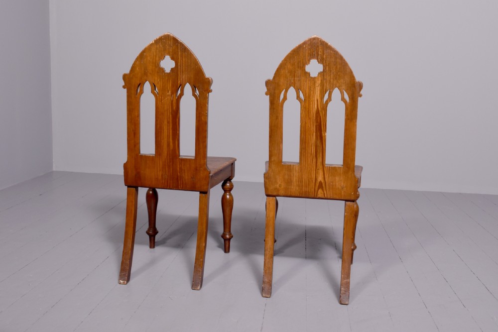 A pair of 19th-century pitch pine Gothic Revival hall chairs with pointed arch backrests, pierced trefoil motifs, turned front legs, and solid timber seats. View III