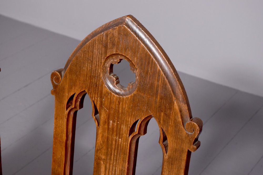 A pair of 19th-century pitch pine Gothic Revival hall chairs with pointed arch backrests, pierced trefoil motifs, turned front legs, and solid timber seats. View IV