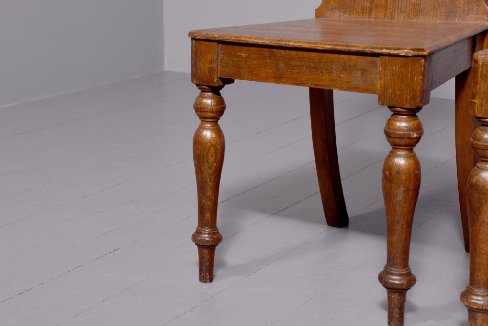 A pair of 19th-century pitch pine Gothic Revival hall chairs with pointed arch backrests, pierced trefoil motifs, turned front legs, and solid timber seats. View V