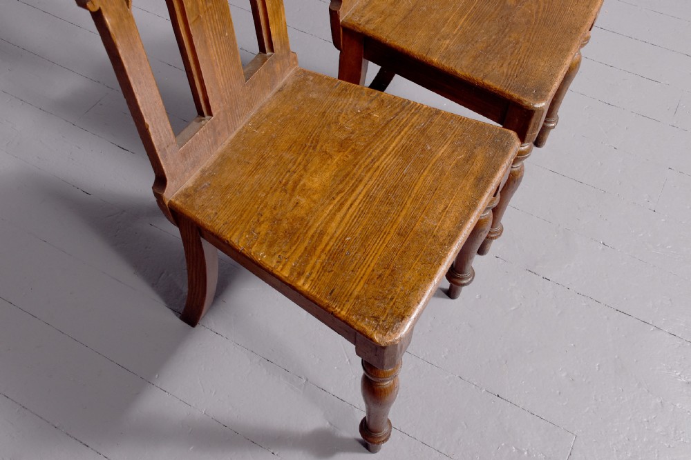 A pair of 19th-century pitch pine Gothic Revival hall chairs with pointed arch backrests, pierced trefoil motifs, turned front legs, and solid timber seats. View VII