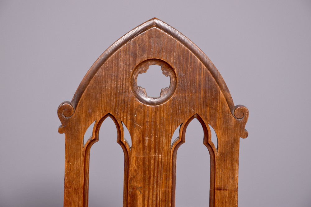 A pair of 19th-century pitch pine Gothic Revival hall chairs with pointed arch backrests, pierced trefoil motifs, turned front legs, and solid timber seats. View VIII