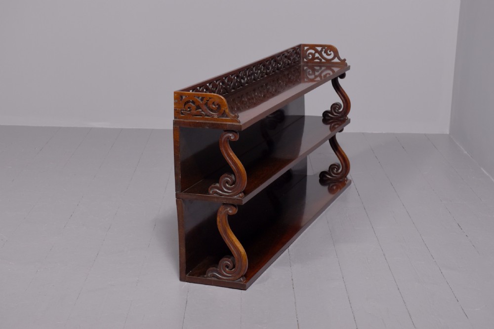A three-tier William IV dark rosewood wall shelf featuring open shelving, curved S-scroll side supports, and a pierced fretwork top gallery rail. View III