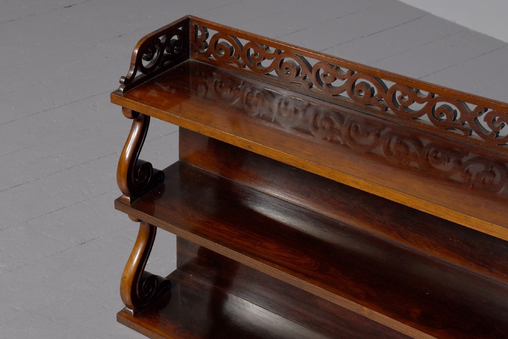 A three-tier William IV dark rosewood wall shelf featuring open shelving, curved S-scroll side supports, and a pierced fretwork top gallery rail. View V