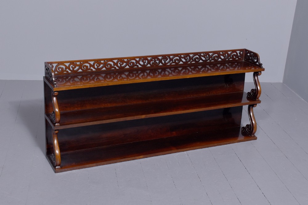 A three-tier William IV dark rosewood wall shelf featuring open shelving, curved S-scroll side supports, and a pierced fretwork top gallery rail. View VI