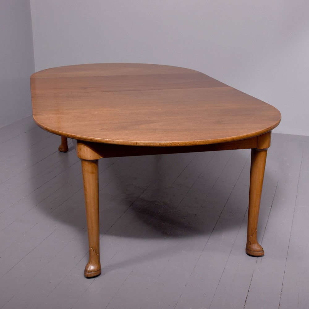 An oval antique timber extending dining table with tapered legs and sculpted pad feet.