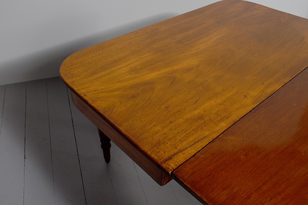 An extendable George IV mahogany dining table featuring a rectangular top with rounded corners, resting on four reeded turned legs with brass castors. View III