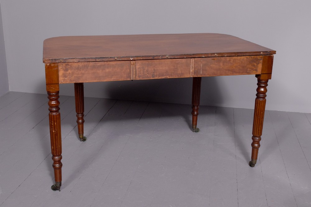 An extendable George IV mahogany dining table featuring a rectangular top with rounded corners, resting on four reeded turned legs with brass castors. View V