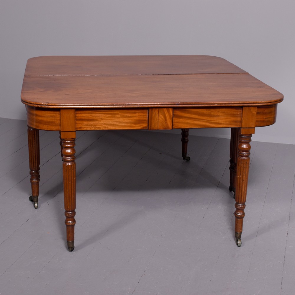 An extendable George IV mahogany dining table featuring a rectangular top with rounded corners, resting on four reeded turned legs with brass castors. View VI