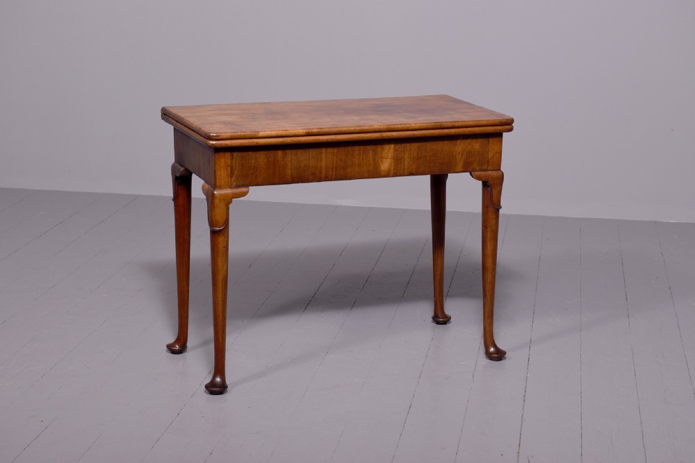 A George II mahogany card table featuring a rectangular fold-over top and slender cabriole legs terminating in pad feet.