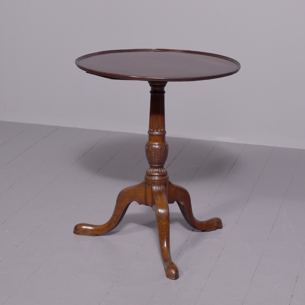 A George III mahogany occasional table featuring a circular top raised on a fluted central pedestal and a tripod base with carved cabriole legs.