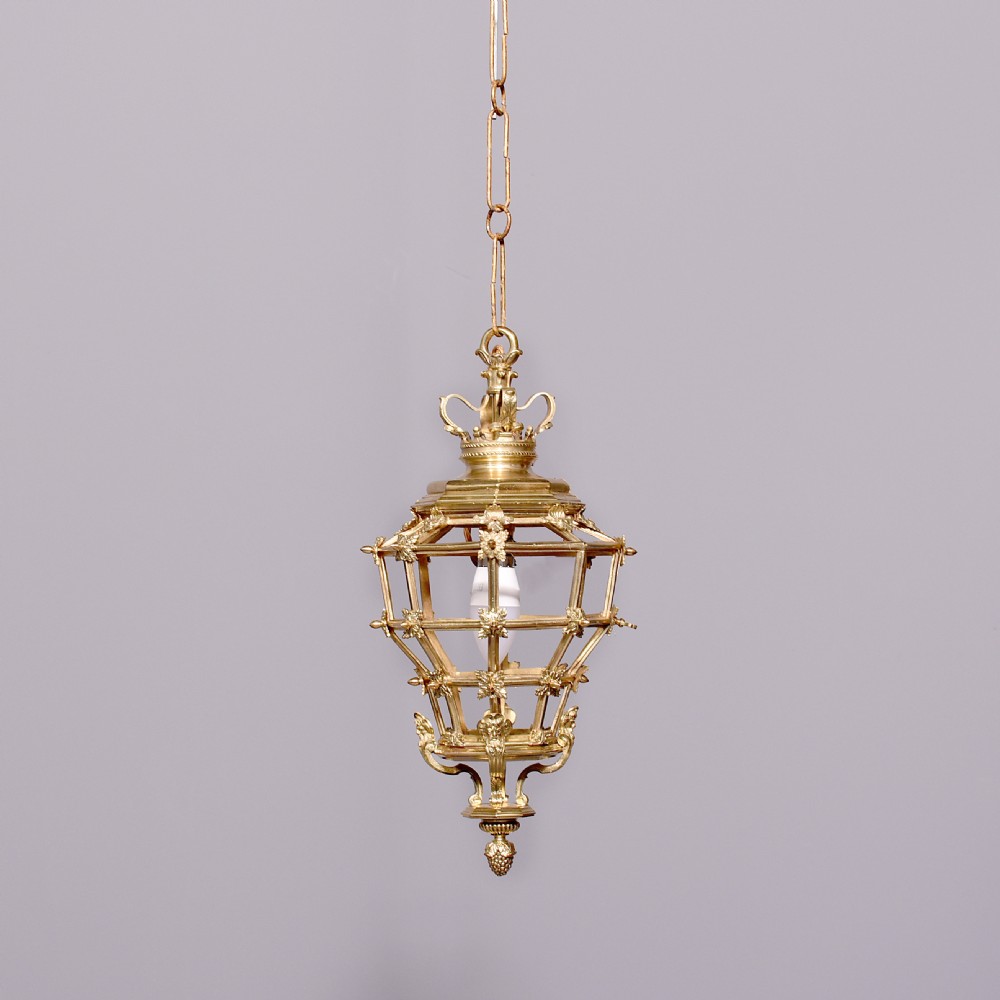 A French hexagonal ormolu ceiling lantern featuring ornate leaf scrollwork, a top crown canopy, and a suspended chain fitting.