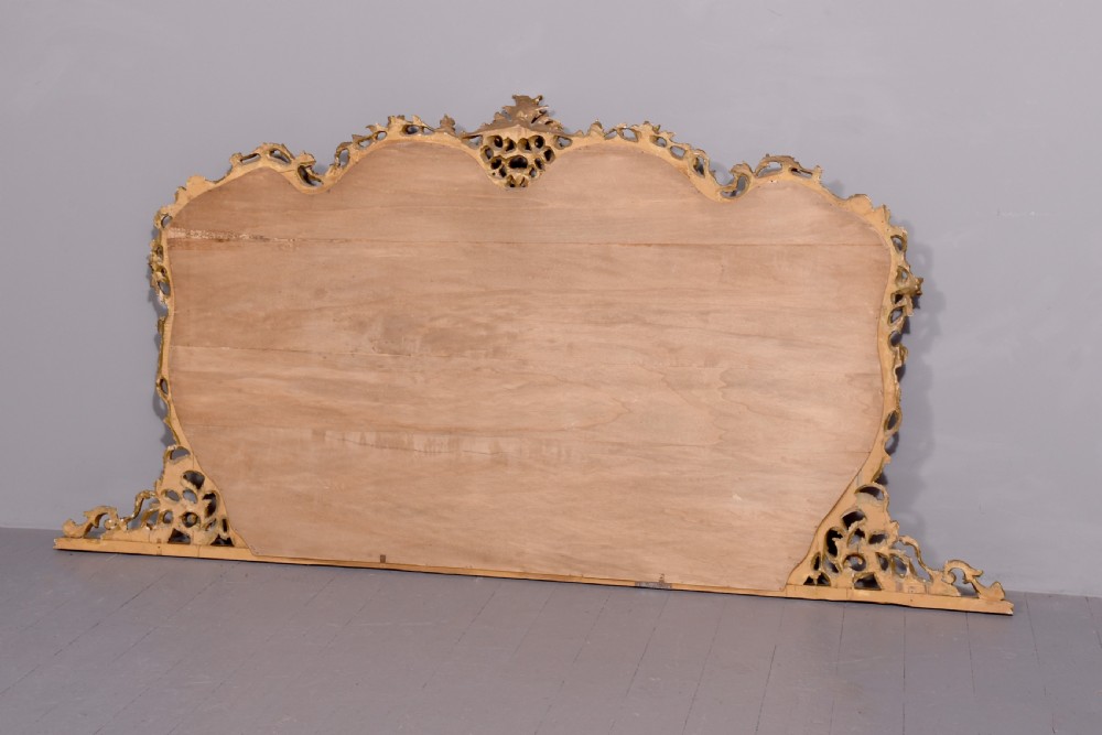 A wide carved giltwood overmantel mirror featuring ornate Rococo scrollwork, acanthus leaf motifs, and an arched cresting. View II
