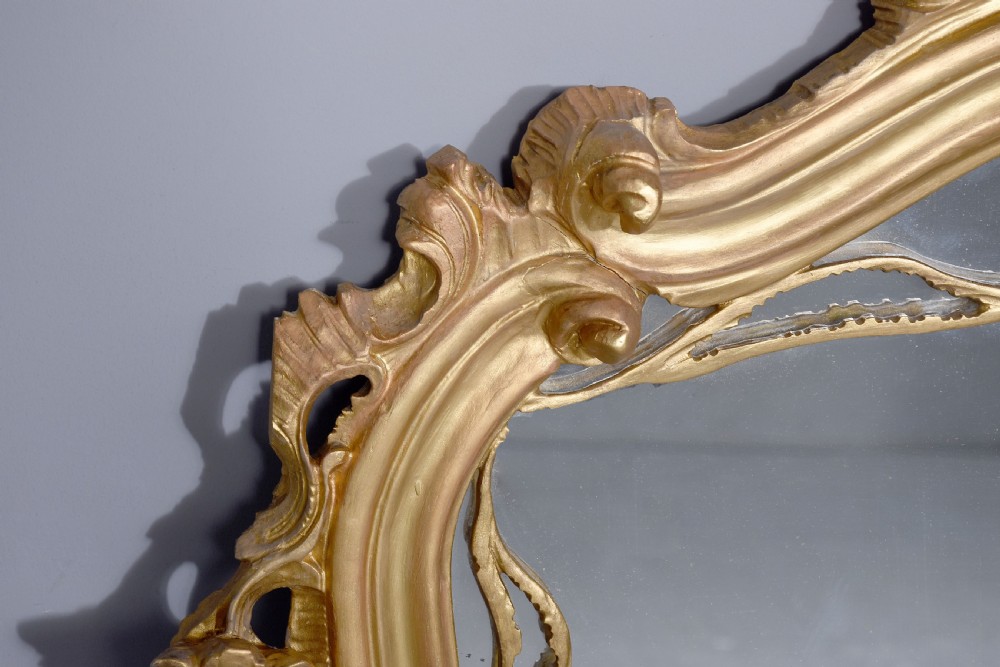 A wide carved giltwood overmantel mirror featuring ornate Rococo scrollwork, acanthus leaf motifs, and an arched cresting. View III