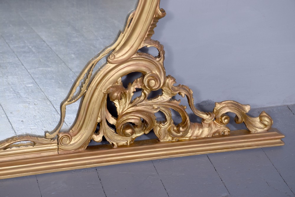 A wide carved giltwood overmantel mirror featuring ornate Rococo scrollwork, acanthus leaf motifs, and an arched cresting. View IV