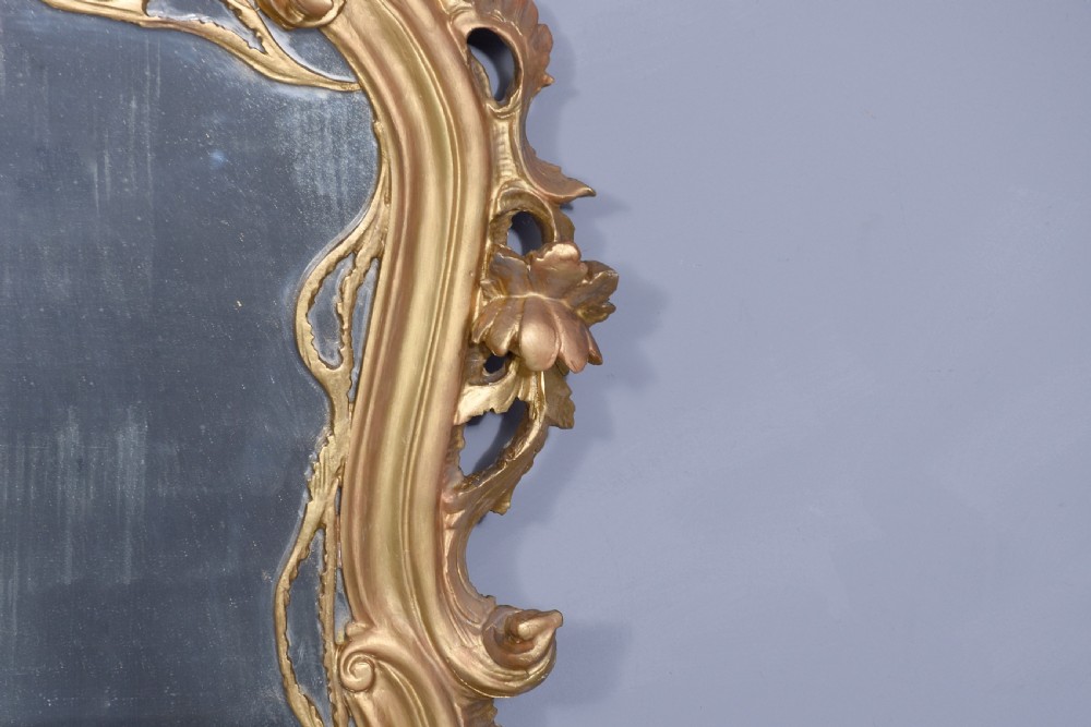 A wide carved giltwood overmantel mirror featuring ornate Rococo scrollwork, acanthus leaf motifs, and an arched cresting. View V