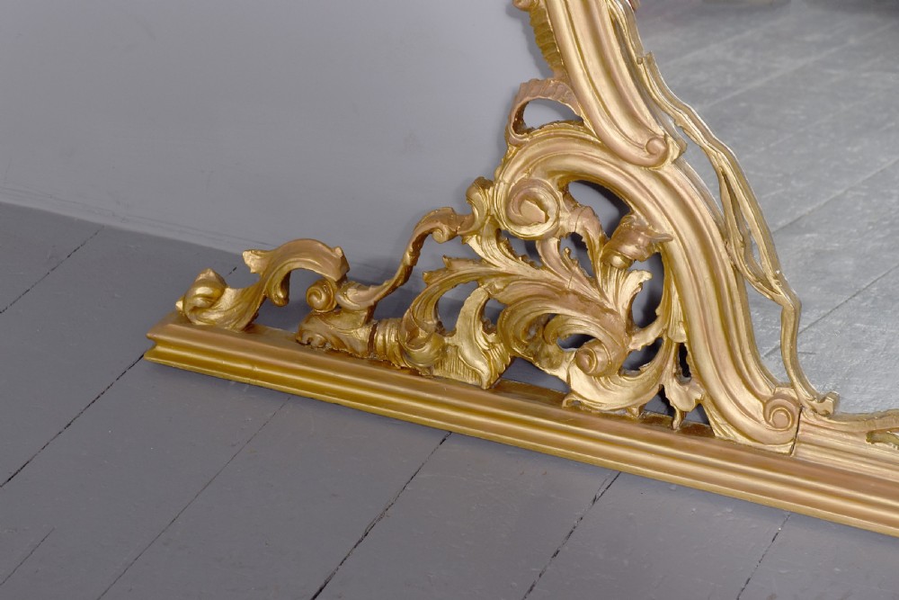 A wide carved giltwood overmantel mirror featuring ornate Rococo scrollwork, acanthus leaf motifs, and an arched cresting. View VII