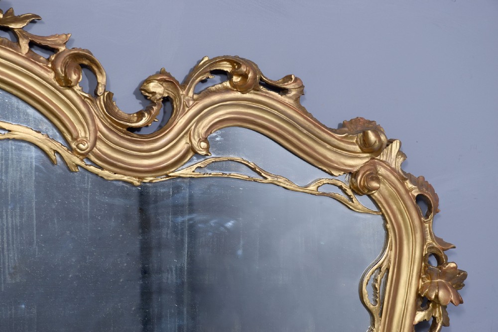 A wide carved giltwood overmantel mirror featuring ornate Rococo scrollwork, acanthus leaf motifs, and an arched cresting. View VIII