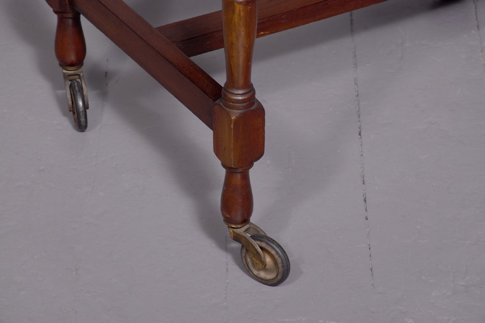 A two-tier mahogany wooden trolley featuring turned upright posts, brass castors, decorative inlay, and scalloped gallery borders. View II